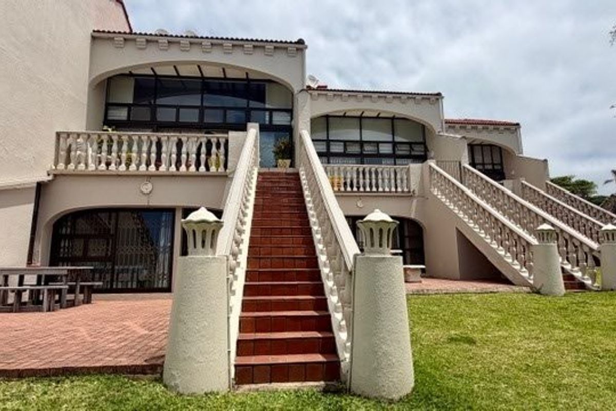 Rear exterior view of a multi-level townhouse featuring arched architectural details, tiled staircases with balustrades, and paved patio areas overlooking a garden.