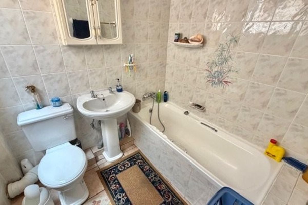 A dated bathroom featuring a standard bathtub, pedestal sink, and toilet with original wall tiling and a medicine cabinet.