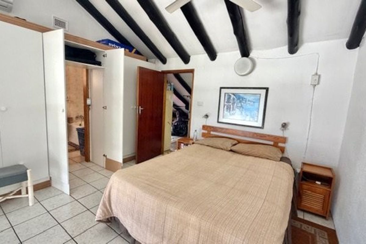 A bedroom featuring exposed dark timber ceiling beams, built-in white cabinetry, and direct access to an en-suite bathroom with tiled flooring.