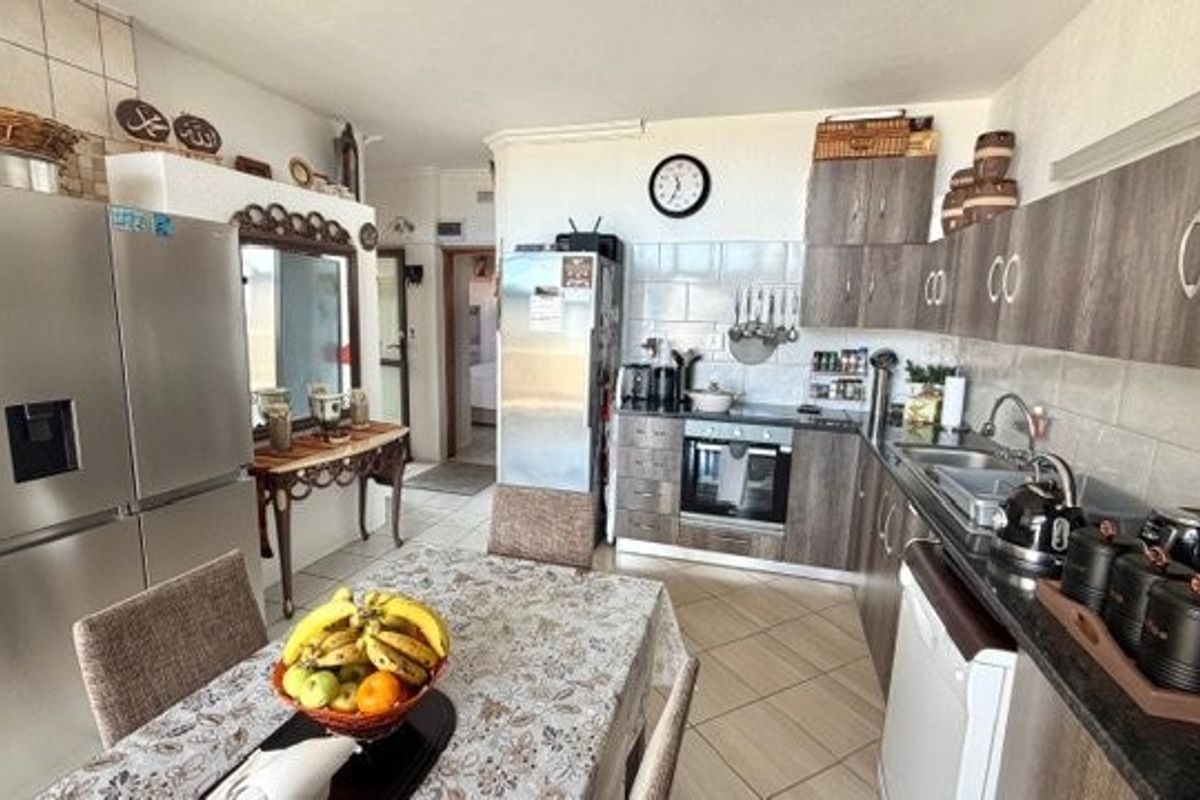 A functional kitchen featuring wood-look cabinetry, tiled splashbacks, built-in oven, and hob, with an adjacent dining area and tiled flooring throughout.
