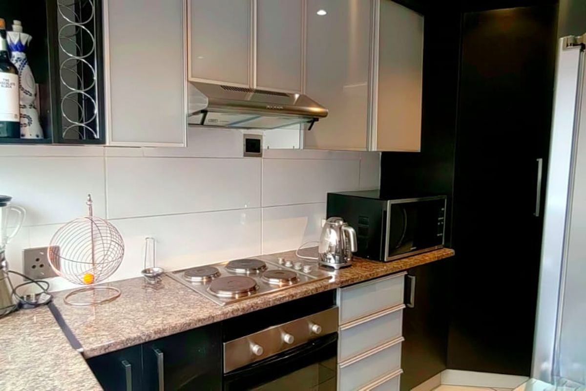 A compact kitchen featuring granite countertops, a built-in oven with electric hob, extractor fan, and modern cabinetry with a tiled splashback.