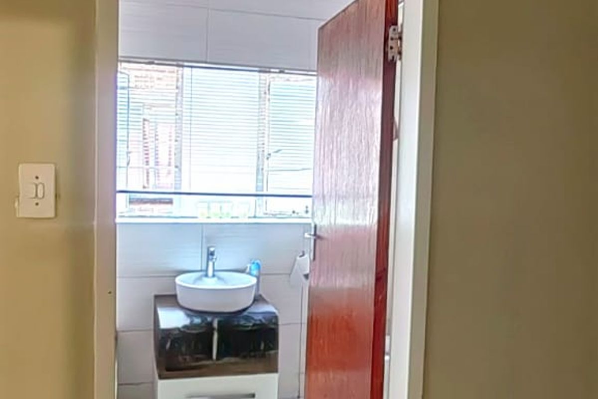 A view into a bathroom featuring a modern vessel sink on a vanity cabinet, tiled walls, and tiled flooring.