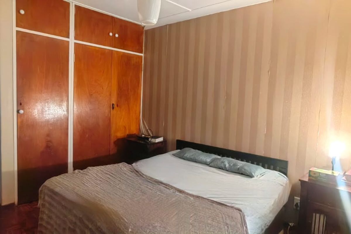 A bedroom featuring built-in wooden cupboards and parquet flooring, currently showing dated finishes and wall treatments.