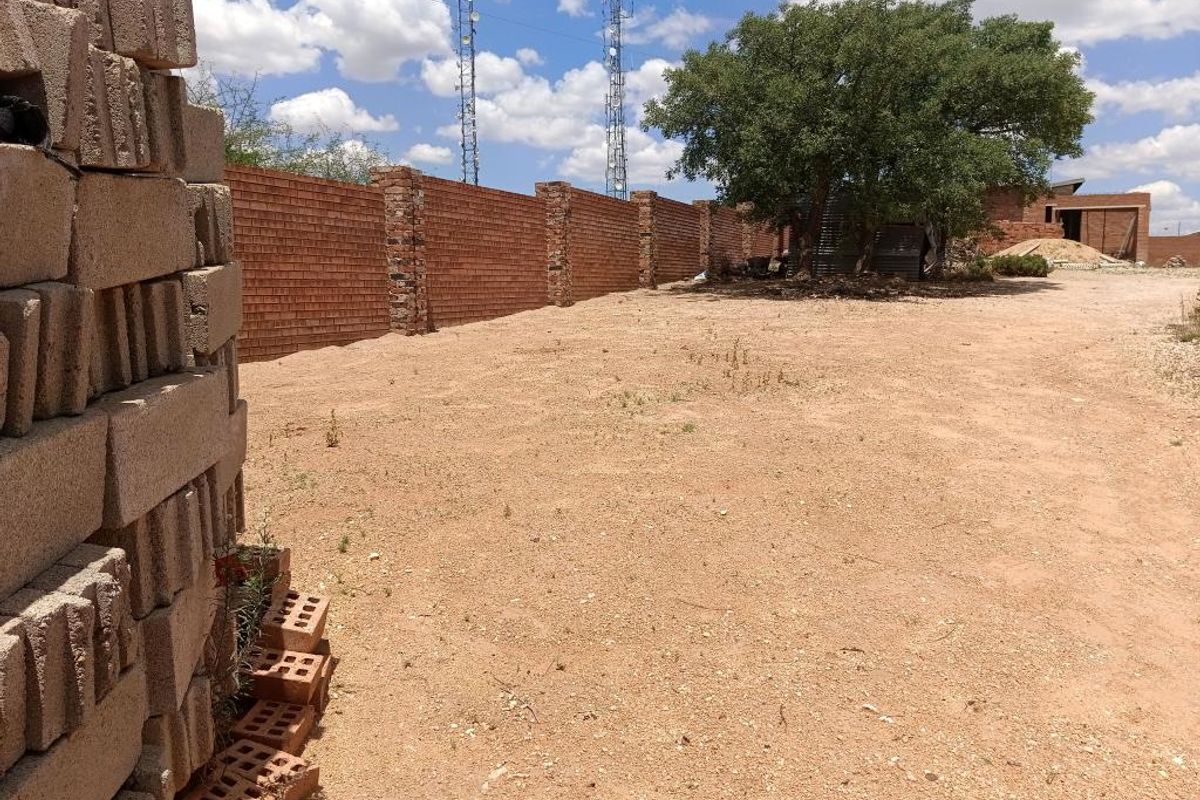 A vacant residential plot featuring a long brick boundary wall and a mature tree, offering a clear space for future development.