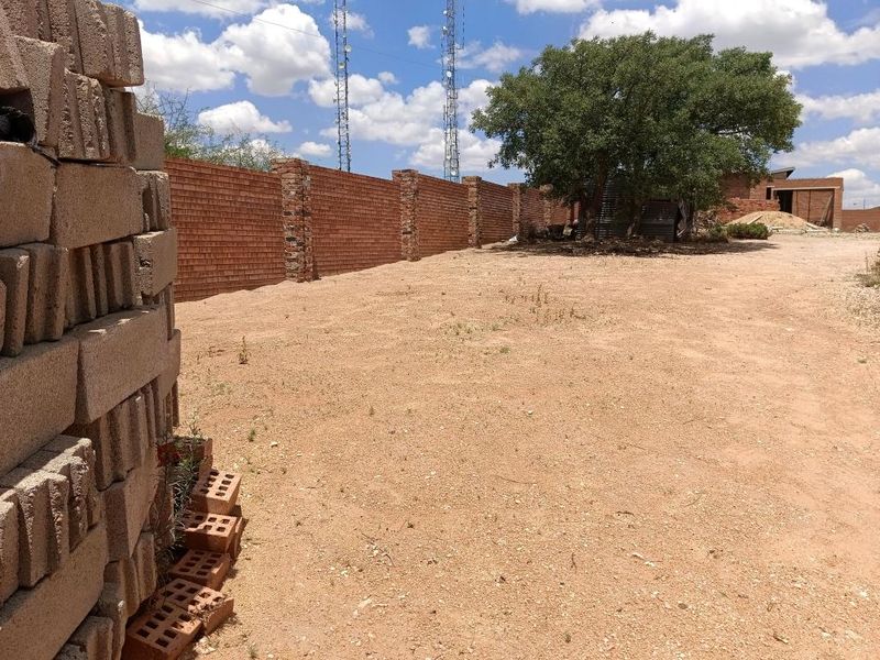 A vacant residential plot featuring a long brick boundary wall and a mature tree, offering a clear space for future development.
