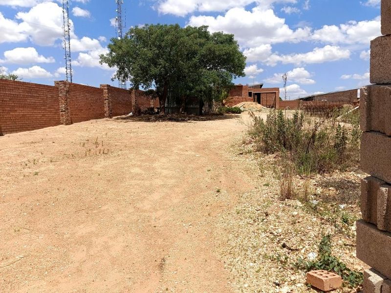 A view of a vacant residential plot featuring a brick boundary wall and a mature tree on the property.