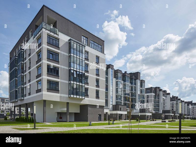 A modern multi-story residential apartment complex featuring contemporary brick and render architecture with glass-enclosed balconies and well-maintained landscaped grounds.