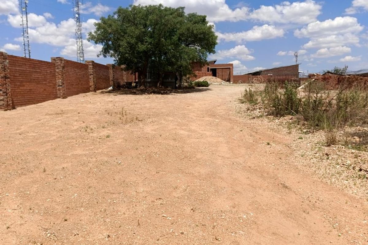 A view of a vacant residential plot featuring a brick boundary wall and a mature tree on the property.