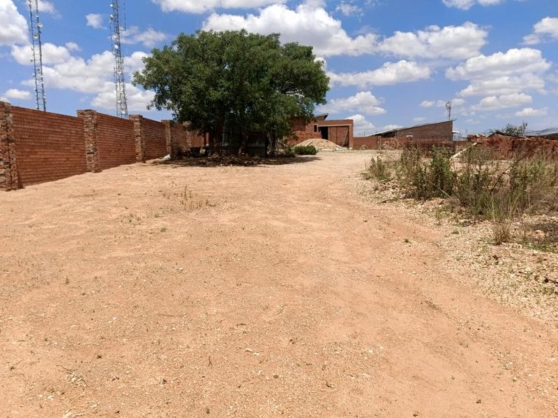 A view of a vacant residential plot featuring a brick boundary wall and a mature tree on the property.