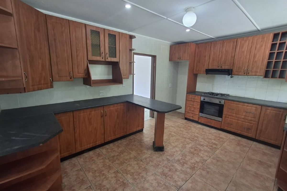 A functional kitchen featuring wood-look cabinetry, dark laminate countertops, a built-in oven, and a gas hob, complemented by tiled flooring.