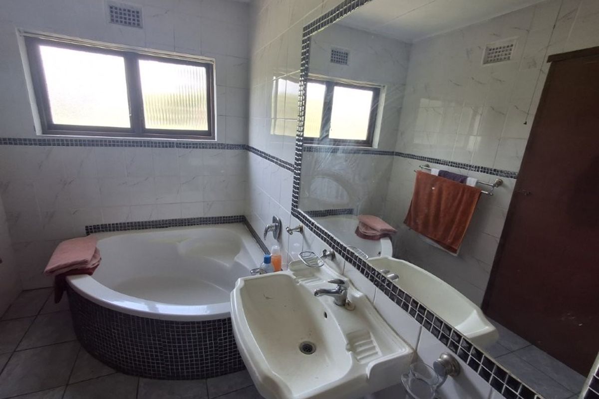 A functional bathroom featuring a corner bathtub, pedestal basin, and large wall-mounted mirror with tiled walls and flooring.
