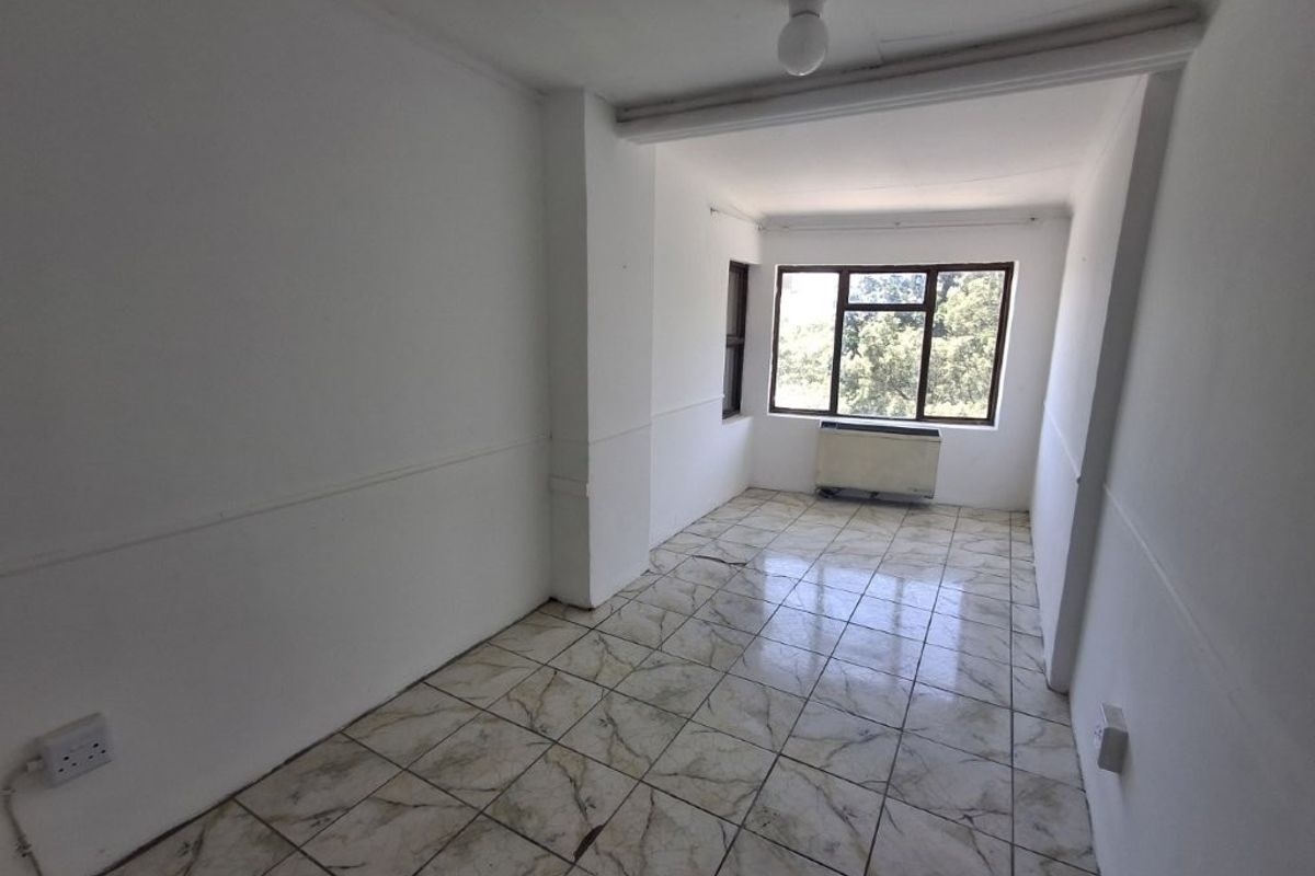 An empty, neutrally painted room featuring tiled flooring, a window with natural light, and a built-in wall-mounted air conditioning unit.