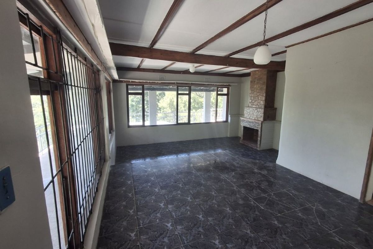 Spacious living room featuring dark tiled flooring, exposed timber ceiling beams, and a stone-clad fireplace, offering a bright and open layout.