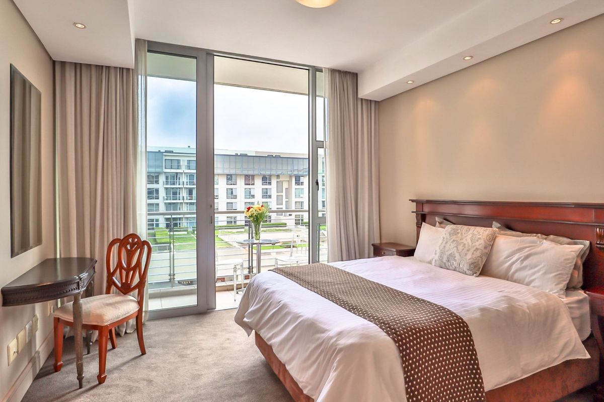 A well-maintained bedroom featuring neutral carpeting, recessed lighting, and a large sliding glass door providing access to a private balcony.