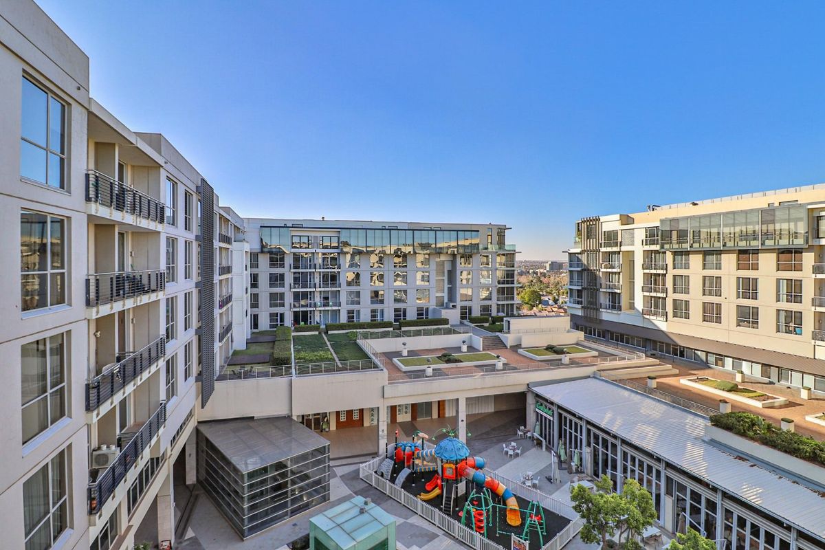 An elevated aerial view of a modern apartment complex featuring landscaped rooftop gardens, paved courtyards, and contemporary architectural design.