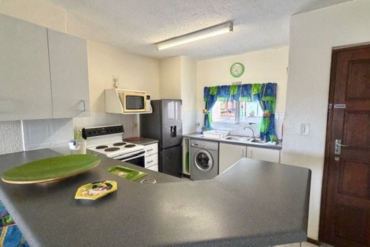 A functional kitchen featuring built-in cabinetry, laminate countertops, an electric stove, and integrated laundry plumbing, offering a practical layout for daily use.