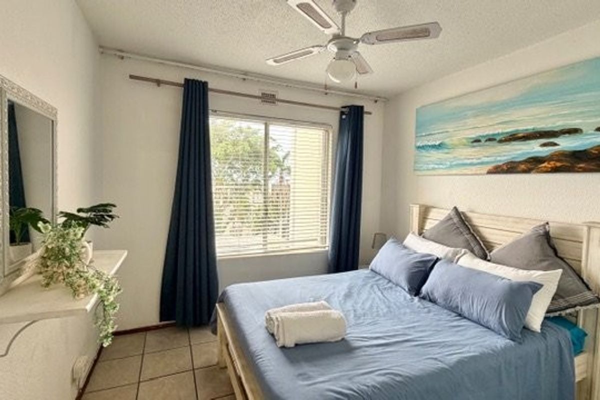 A functional bedroom featuring tiled flooring, a ceiling fan, and a window with blinds, providing a comfortable and well-lit sleeping space.