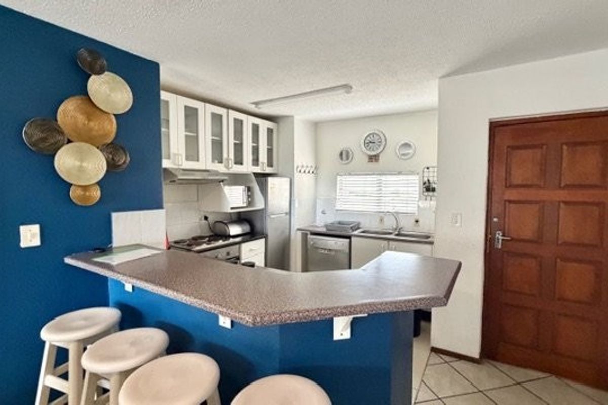 Functional kitchen featuring a breakfast bar, ample cabinetry, built-in oven, cooktop, and stainless steel sink, with tiled flooring throughout.