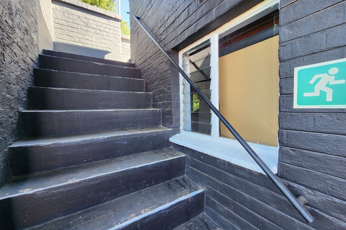 Exterior staircase with dark painted brickwork, metal handrail, and a boarded-up window section.