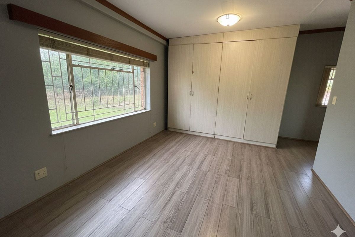 A bright, empty bedroom featuring wood-look laminate flooring, built-in wardrobes, and large windows with security bars.