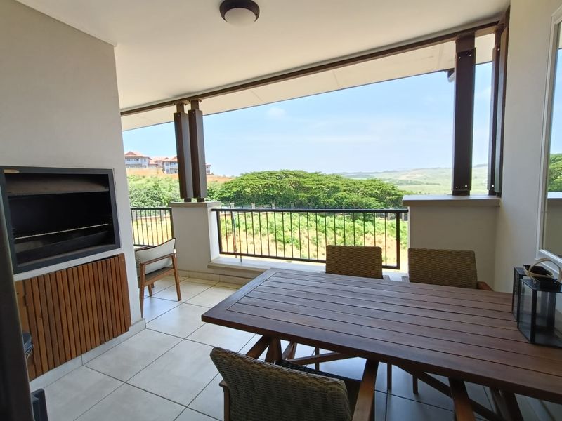 Covered balcony featuring a built-in braai, tiled flooring, and metal balustrade, offering scenic views of the surrounding landscape.