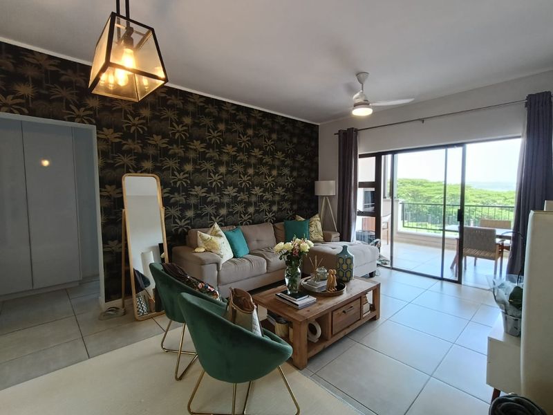 A well-maintained living room featuring tiled floors, a ceiling fan, and large sliding glass doors that open onto a balcony with scenic views.