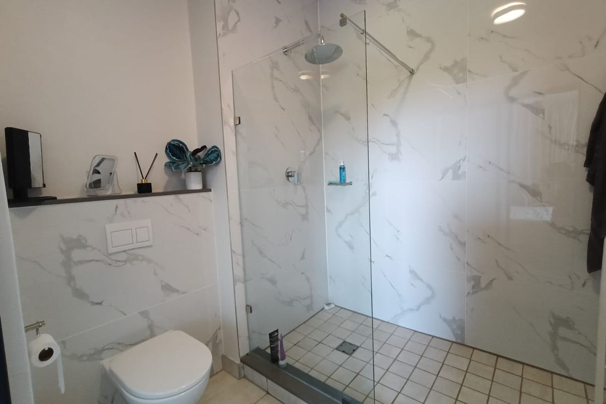 Modern bathroom featuring a walk-in shower with glass screen, rainfall shower head, and elegant marble-look wall tiles with a wall-mounted toilet.