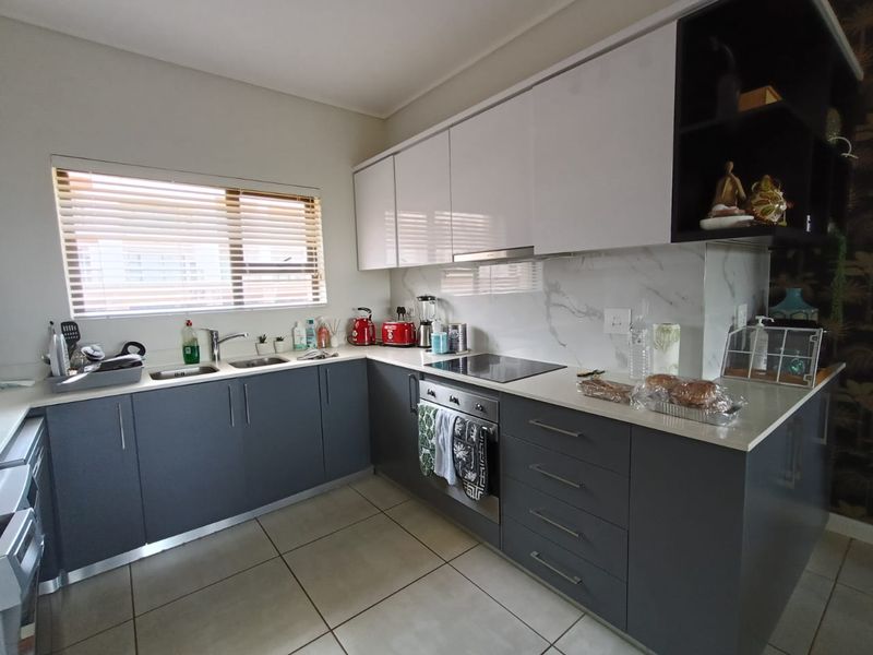 Modern kitchen featuring sleek grey lower cabinetry, white upper cabinets, stone countertops, marble-look splashback, and integrated stainless steel appliances.