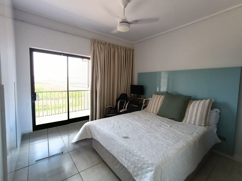 A bright bedroom featuring tiled flooring, a ceiling fan, and a large sliding glass door providing access to a balcony with scenic views.