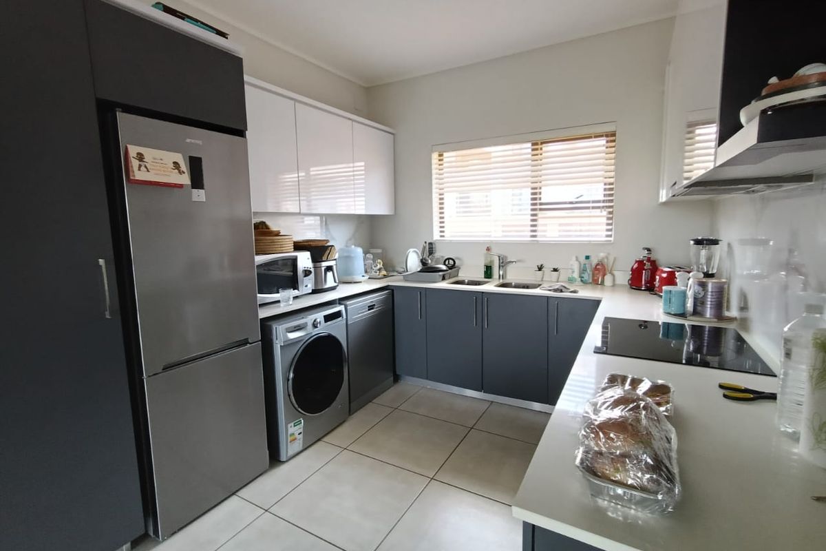 Modern kitchen featuring sleek grey and white cabinetry, stone countertops, integrated appliances, and tiled flooring with ample natural light.