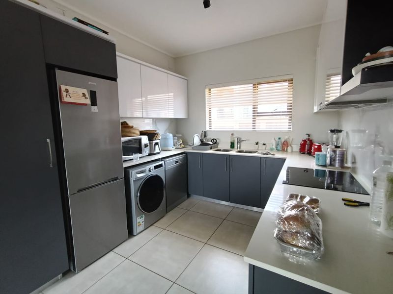 Modern kitchen featuring sleek grey and white cabinetry, stone countertops, integrated appliances, and tiled flooring with ample natural light.