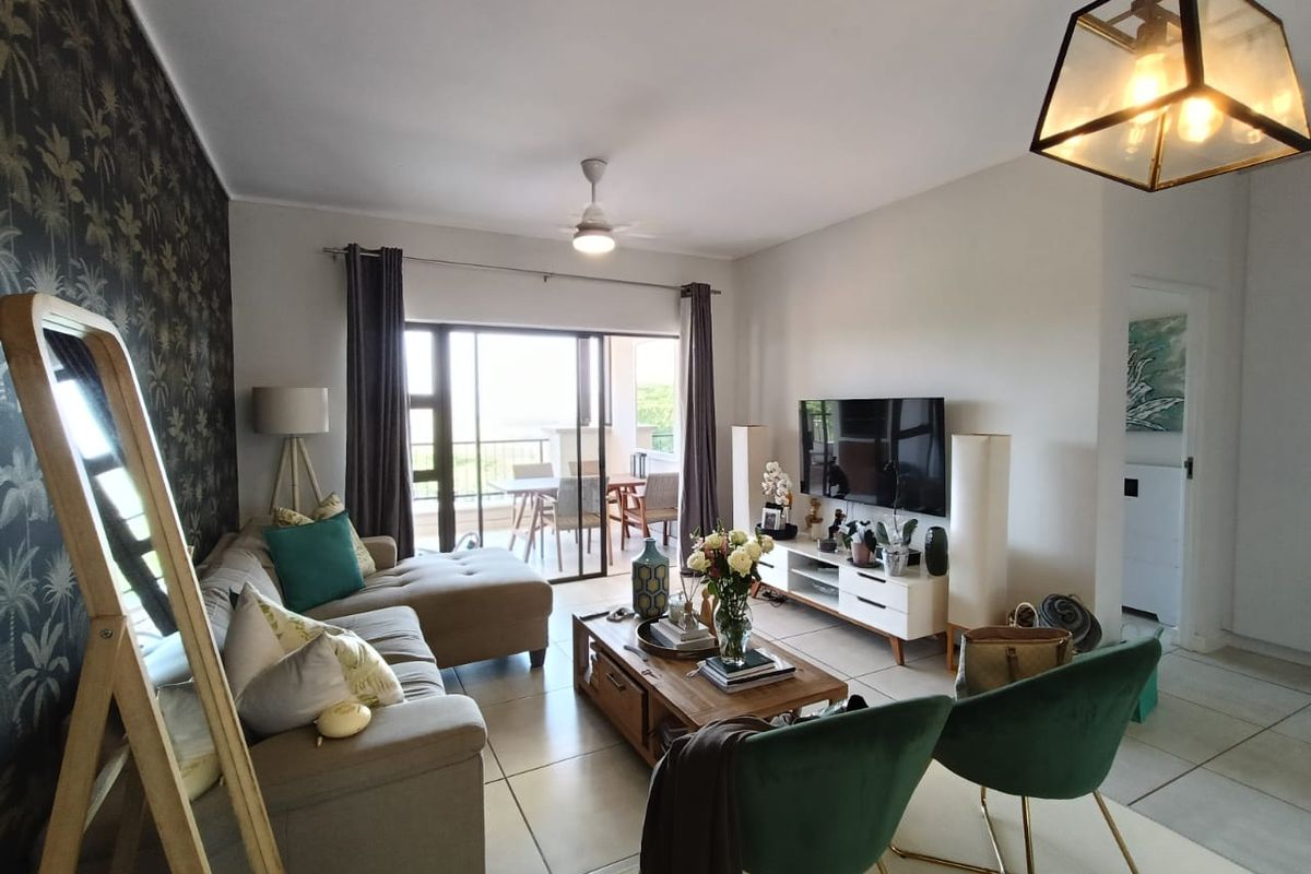 A well-maintained living room featuring tiled flooring, a ceiling fan, and a large sliding glass door providing access to an outdoor patio area.