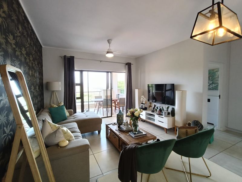 A well-maintained living room featuring tiled flooring, a ceiling fan, and a large sliding glass door providing access to an outdoor patio area.