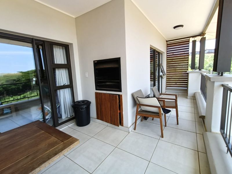 A spacious covered balcony featuring tiled flooring, a built-in braai, and a timber privacy screen, offering a functional outdoor entertainment area.