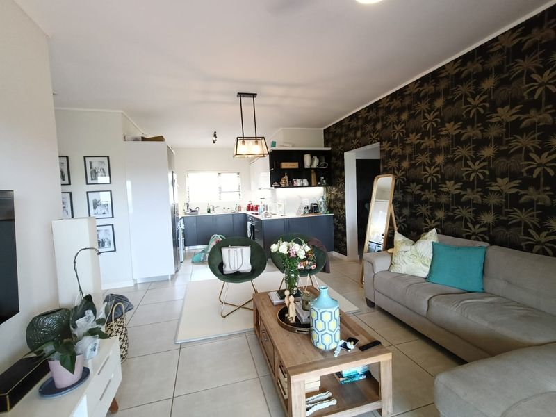 An open-plan living and kitchen area featuring tiled flooring, modern dark kitchen cabinetry, and a feature wallpaper wall.