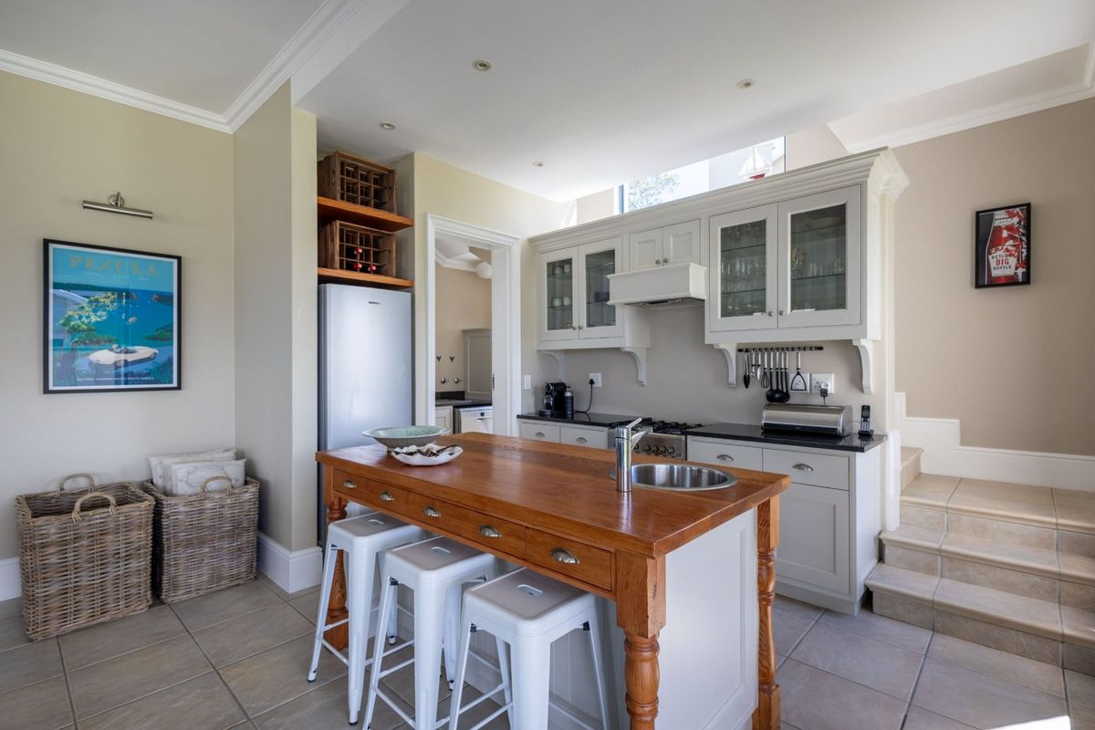 A well-appointed kitchen featuring a central timber-topped island with a prep sink, custom cabinetry, and integrated appliances, finished with neutral tiling.