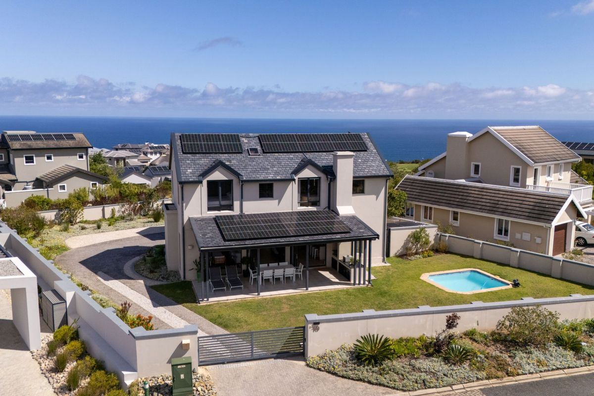 Aerial view of a modern two-story residence featuring a slate roof with integrated solar panels, a covered patio, swimming pool, and landscaped garden.