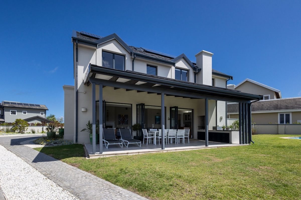 Rear view of a two-story house featuring a covered patio with built-in braai, bi-fold doors, and a landscaped garden.