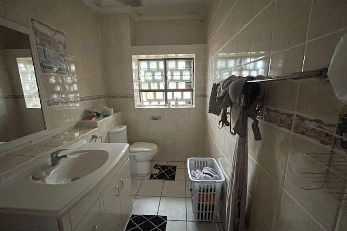A functional bathroom featuring a vanity cabinet, toilet, and tiled finishes, currently showing signs of ceiling water damage requiring maintenance.