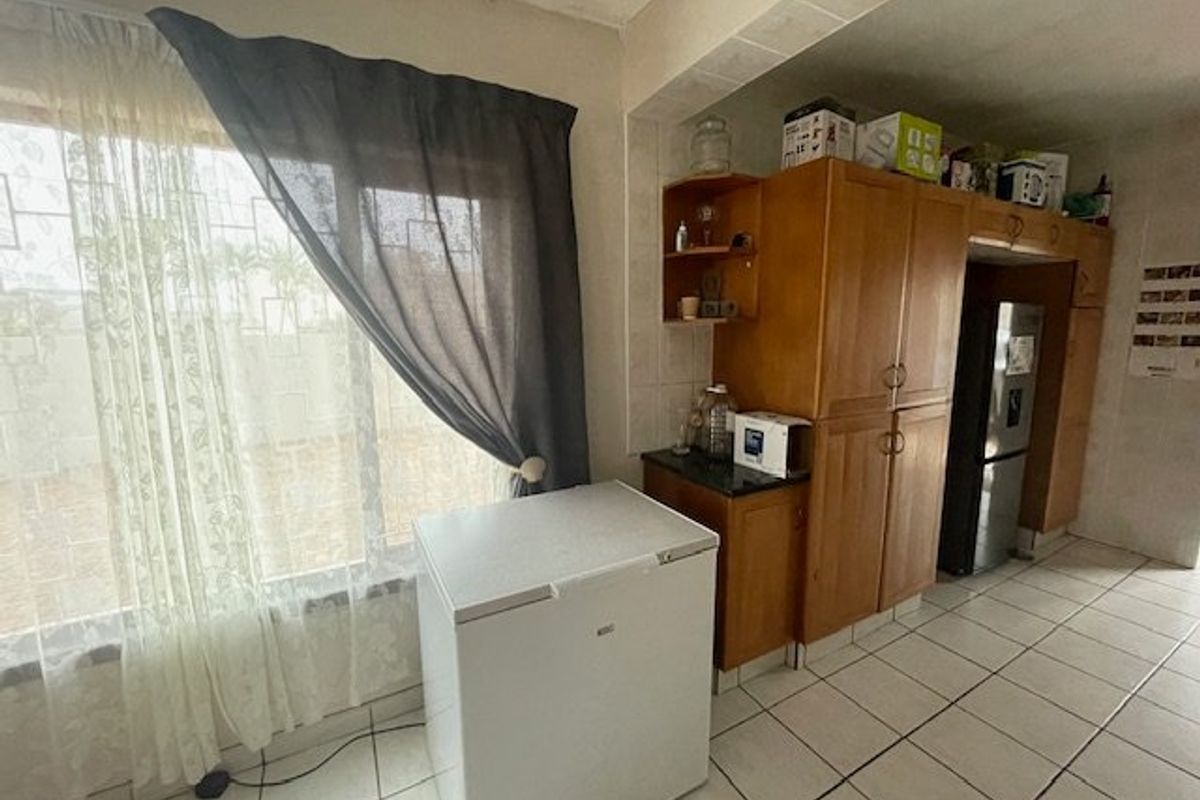 Kitchen area featuring built-in wooden cabinetry, tiled flooring, and a large window with security bars.