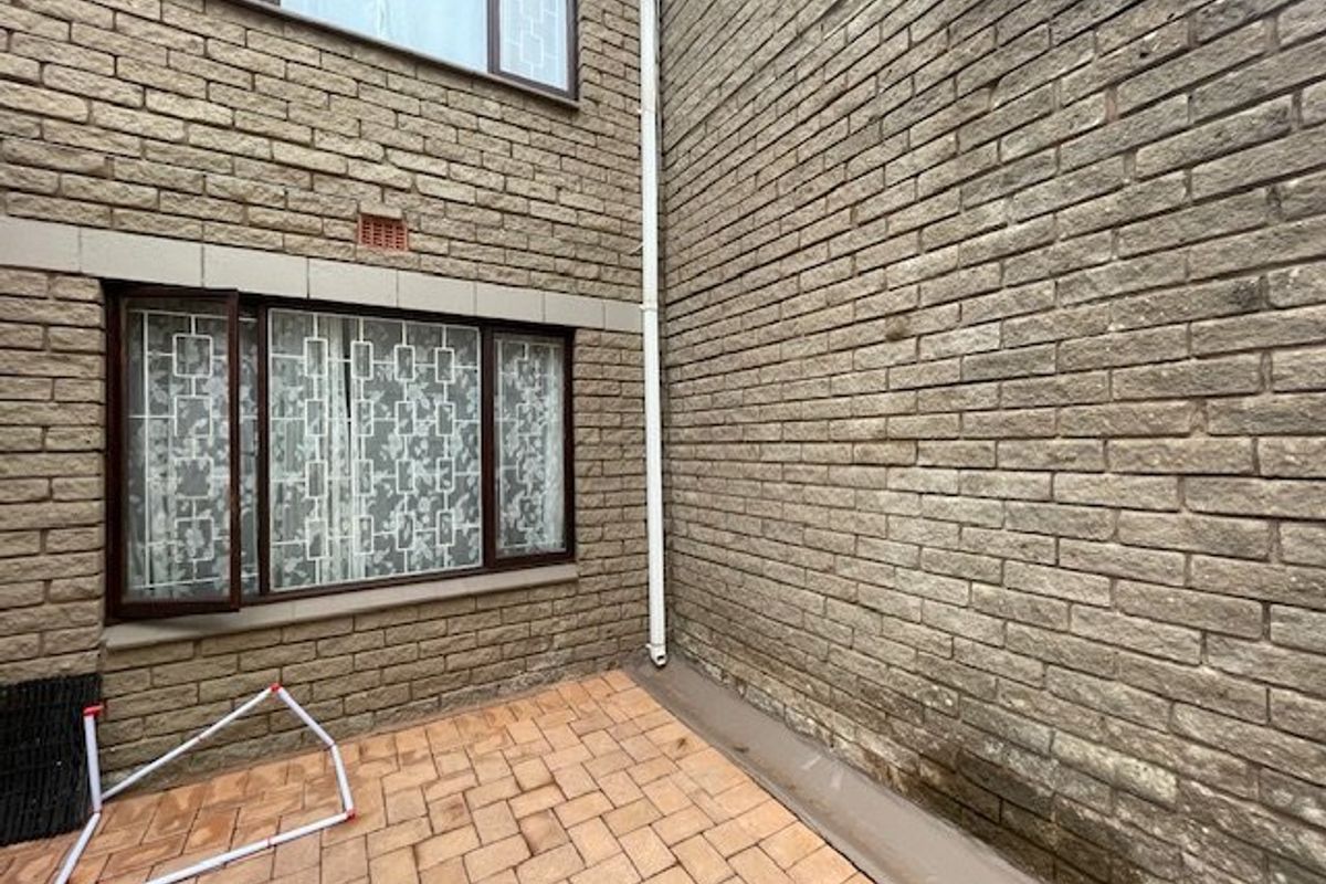 A rear exterior view of the townhouse featuring a paved patio area and brick facade with visible signs of weathering and damp.