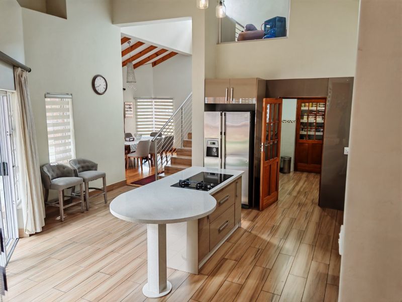 Spacious open-plan living area featuring a modern kitchen island with integrated hob, wood-look tile flooring, and a striking timber staircase under vaulted ceilings.