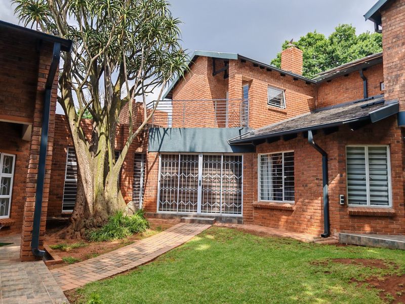 Rear view of a face brick house featuring a paved garden path, upper-level balcony, and secure metal window and door fixtures.