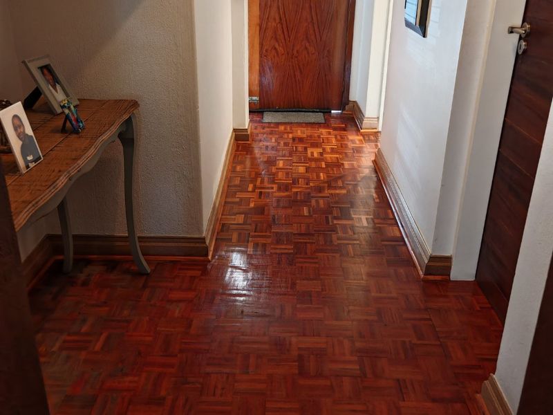 A welcoming entrance hall featuring polished parquet flooring and a solid wooden front door, leading into the home's interior.