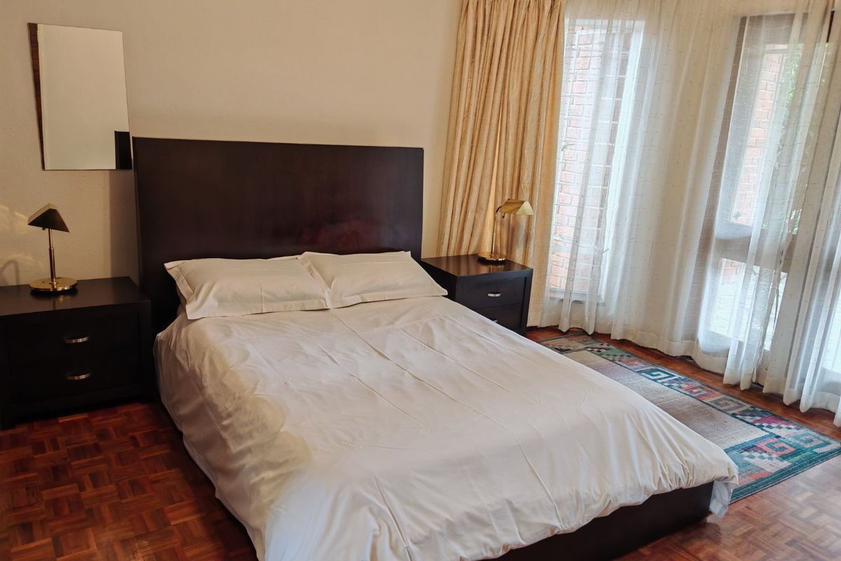A bedroom featuring classic parquet flooring and a large bay window with curtains, providing natural light and a traditional aesthetic.