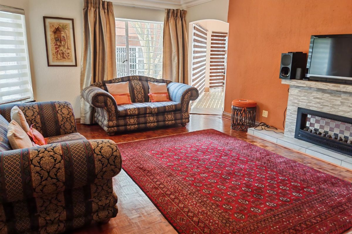A comfortable living room featuring parquet flooring, a stone-clad fireplace, and natural light through large windows with access to an adjacent space.