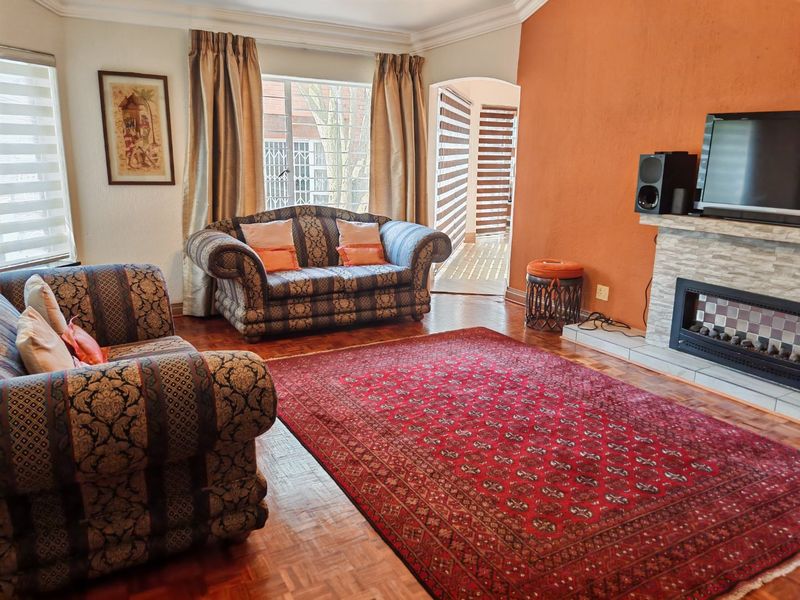 A comfortable living room featuring parquet flooring, a stone-clad fireplace, and natural light through large windows with access to an adjacent space.