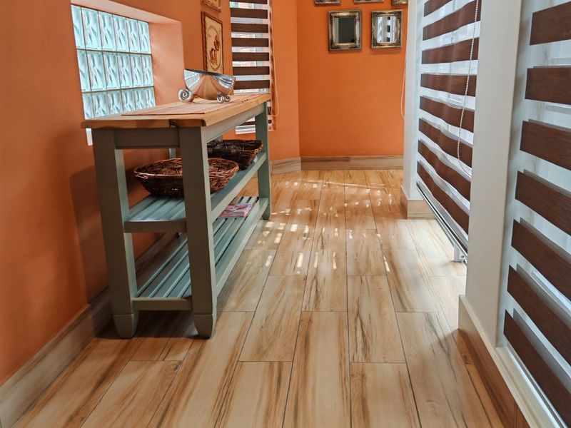 A bright hallway featuring wood-look tile flooring, glass block windows, and modern roller blinds, creating a warm and inviting transition space.