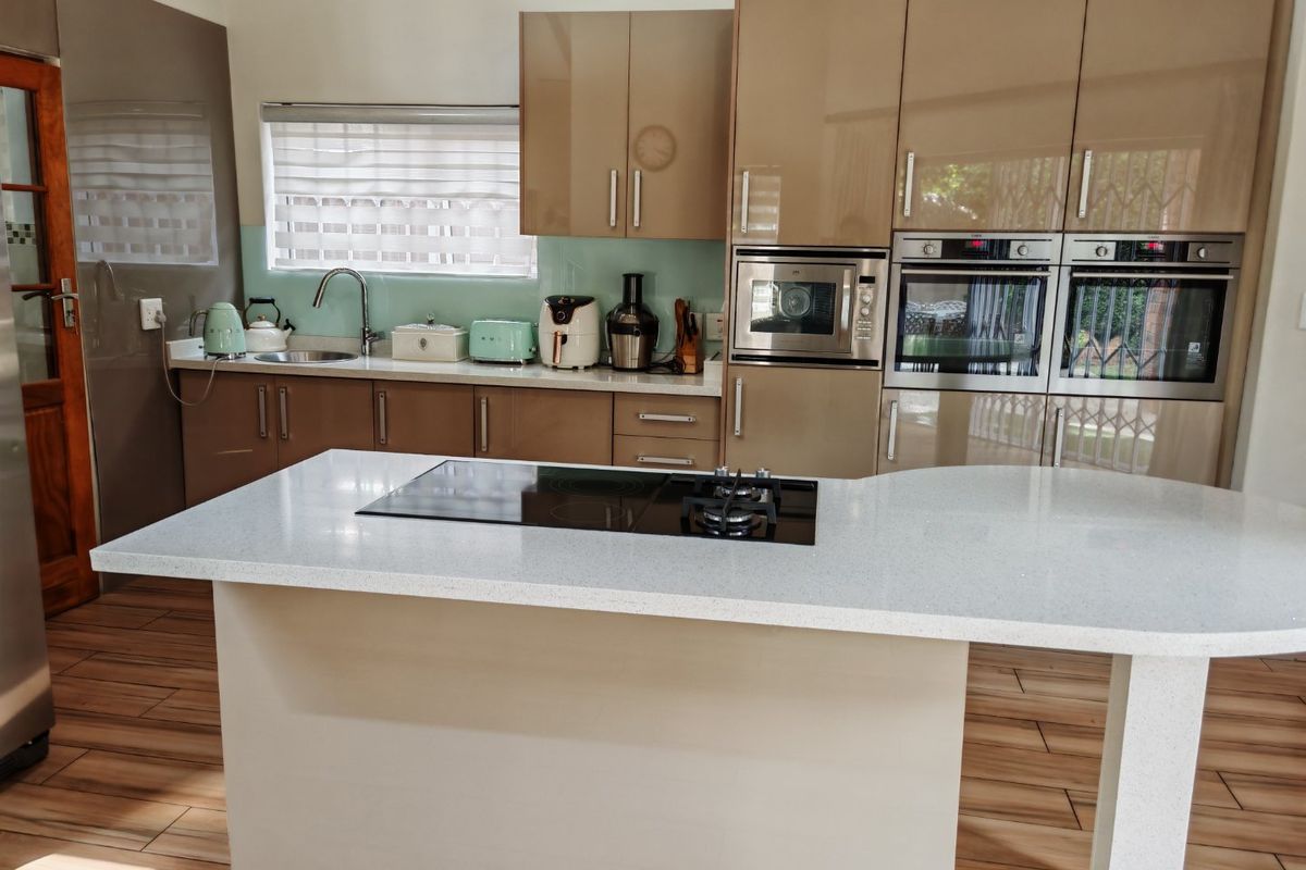 Modern kitchen featuring high-gloss cabinetry, a central island with integrated hob, stone countertops, and built-in double ovens.