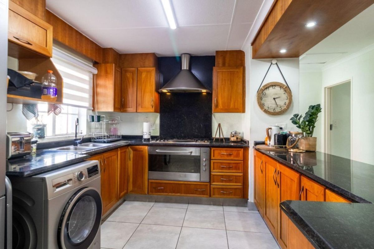 A well-maintained kitchen featuring warm wooden cabinetry, dark granite countertops, a stainless steel extractor fan, and a built-in oven with gas hob.